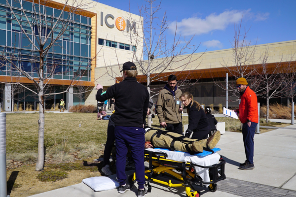 Emergency responders practice a rescue outside a modern building. A person lies on a stretcher as others gather, conveying a sense of urgency and teamwork.