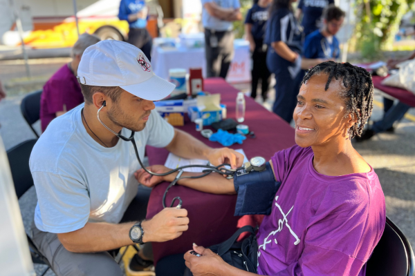 A healthcare worker checks a smiling woman's blood pressure outdoors at a community health event.